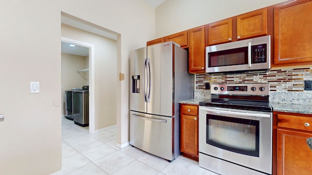 kitchen with light stone countertops, washer and clothes dryer, light tile patterned floors, and appliances with stainless steel finishes