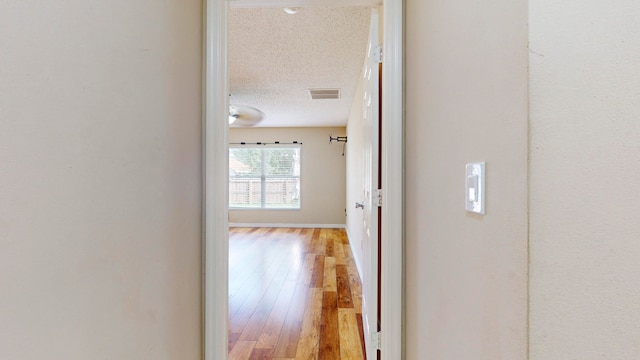 hallway with light hardwood / wood-style floors and a textured ceiling