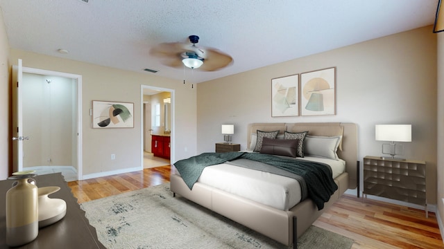 bedroom featuring ceiling fan, ensuite bathroom, a textured ceiling, and light wood-type flooring