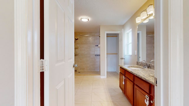 bathroom with tile patterned flooring, a tile shower, vanity, and a textured ceiling