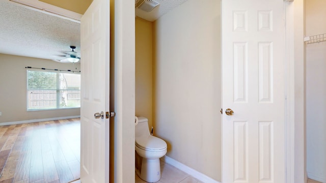 bathroom with hardwood / wood-style floors, ceiling fan, toilet, and a textured ceiling