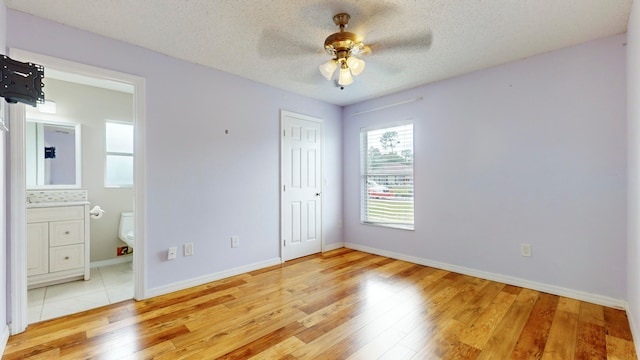 unfurnished bedroom with ensuite bath, ceiling fan, hardwood / wood-style floors, and a textured ceiling