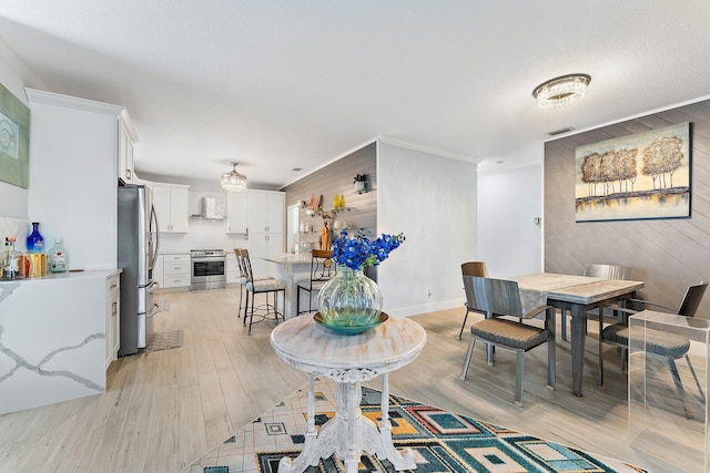 dining area featuring light hardwood / wood-style flooring, wood walls, and ornamental molding