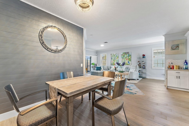 dining room with wooden walls, light wood-type flooring, and crown molding