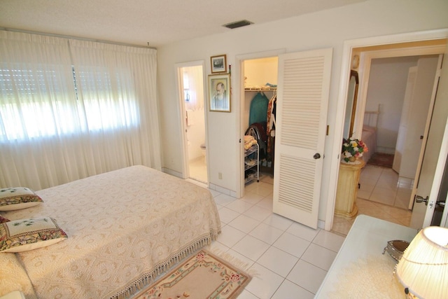 tiled bedroom with connected bathroom, a spacious closet, and a closet