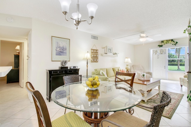 dining space with a textured ceiling, ceiling fan with notable chandelier, and light tile patterned floors