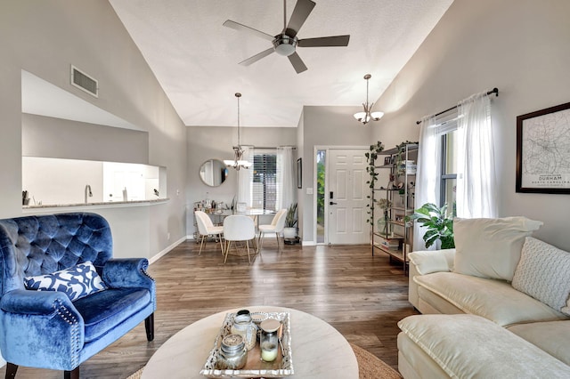 living room with ceiling fan with notable chandelier, a wealth of natural light, high vaulted ceiling, and dark wood-type flooring