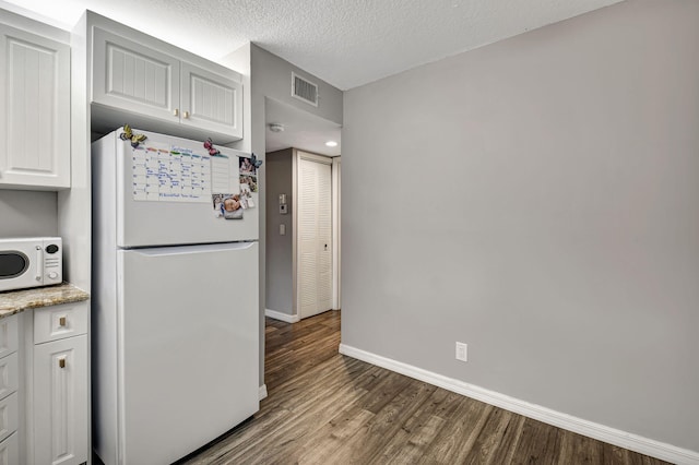 kitchen featuring light stone counters, white cabinets, white appliances, a textured ceiling, and hardwood / wood-style flooring