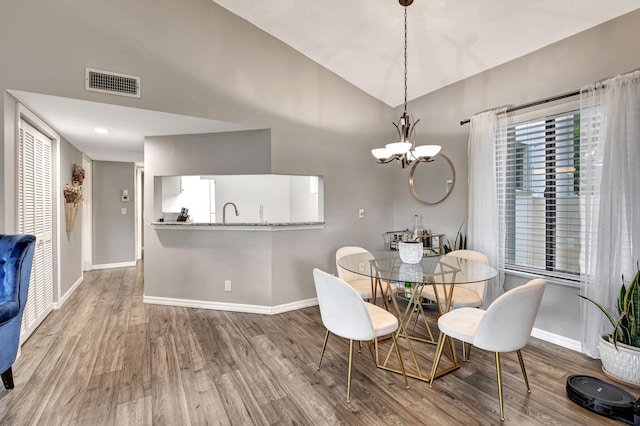 dining space featuring wood-type flooring, an inviting chandelier, lofted ceiling, and sink