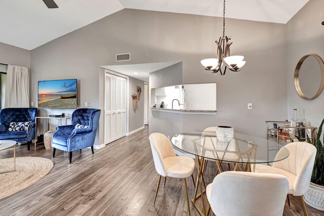 dining room featuring hardwood / wood-style floors, high vaulted ceiling, sink, and a notable chandelier