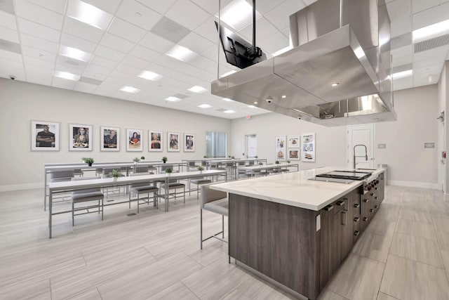 kitchen with a spacious island, stainless steel gas cooktop, a drop ceiling, dark brown cabinetry, and light stone counters