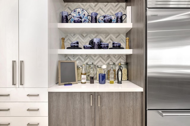 bar with stainless steel fridge, white cabinetry, and tasteful backsplash