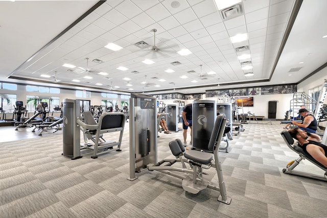 gym featuring light carpet, a paneled ceiling, a tray ceiling, and ceiling fan