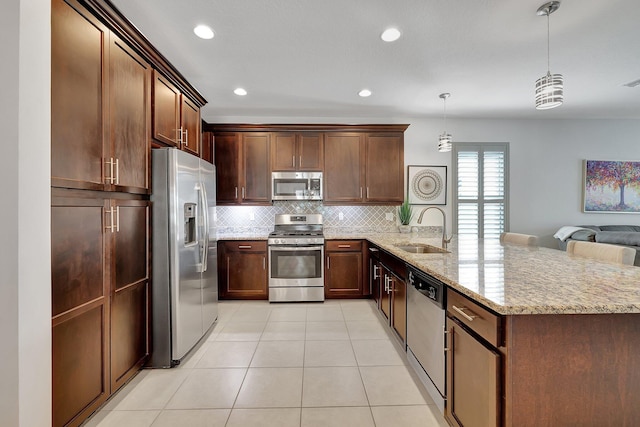 kitchen with kitchen peninsula, hanging light fixtures, light stone countertops, sink, and stainless steel appliances