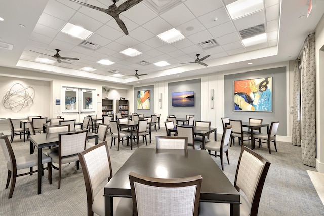 dining area featuring a drop ceiling, ceiling fan, light colored carpet, and a raised ceiling