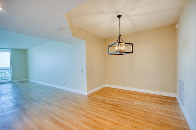 empty room with a chandelier, light wood finished floors, visible vents, and baseboards