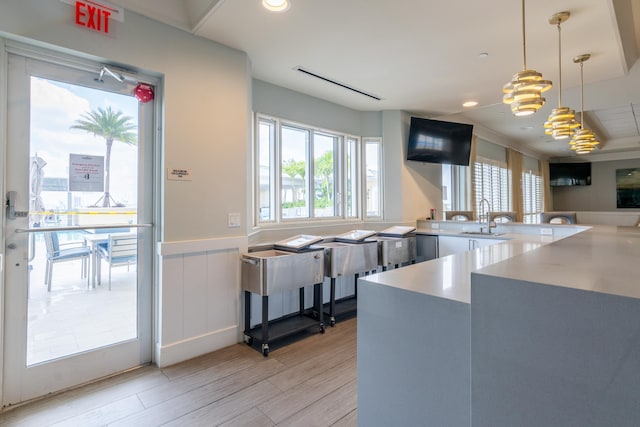 kitchen with light wood-style flooring, a sink, light countertops, wainscoting, and pendant lighting