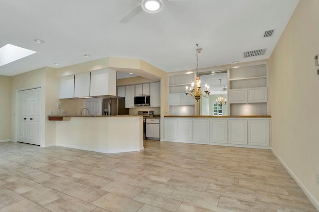 kitchen with appliances with stainless steel finishes, white cabinets, ceiling fan with notable chandelier, kitchen peninsula, and a skylight