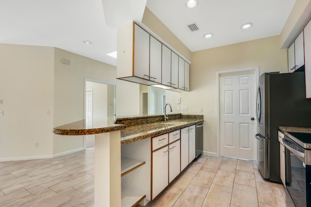 kitchen with white cabinets, sink, kitchen peninsula, stainless steel appliances, and dark stone countertops