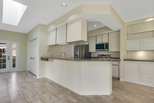 kitchen with dark stone countertops, kitchen peninsula, stainless steel appliances, a skylight, and sink