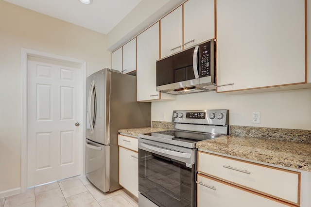 kitchen with stainless steel appliances, white cabinetry, light stone counters, and light tile patterned flooring