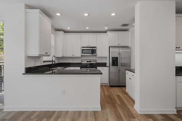 kitchen with stainless steel appliances, white cabinets, kitchen peninsula, and light hardwood / wood-style floors