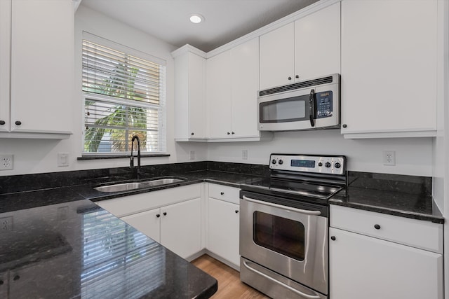 kitchen with stainless steel appliances, white cabinets, dark stone countertops, and sink