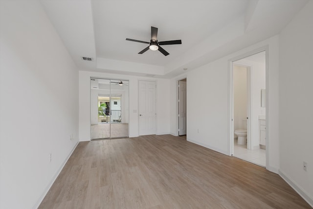 empty room with ceiling fan, light wood-type flooring, and a tray ceiling