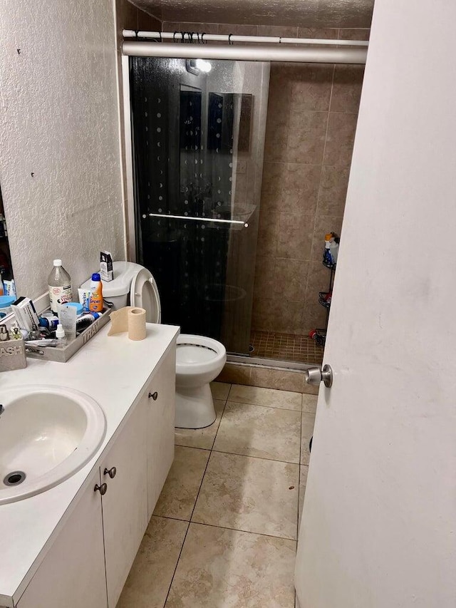 bathroom with tile patterned flooring, vanity, toilet, and a shower with door