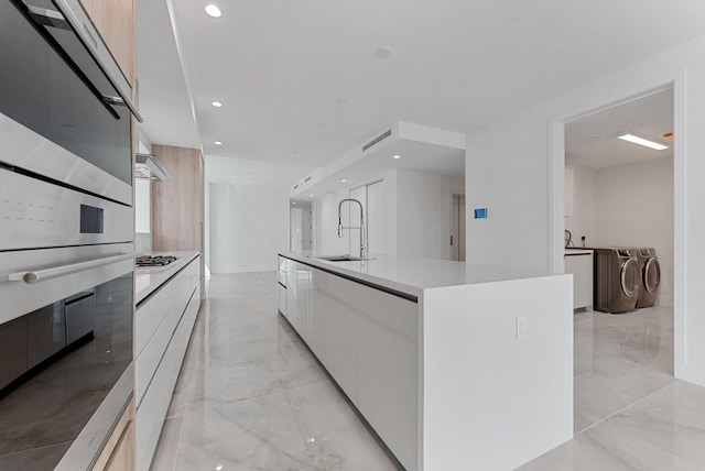 485 E Royal Palm Rd Unit 204, Boca Raton, FL 33432 - kitchen featuring modern cabinets, separate washer and dryer, a sink, light marble finish flooring, and white cabinetry