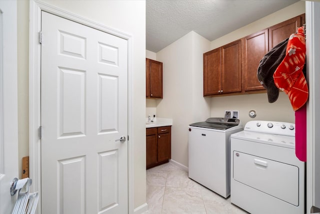 laundry area with a textured ceiling, separate washer and dryer, light tile patterned floors, and cabinets