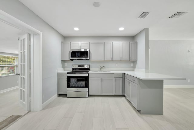 kitchen with appliances with stainless steel finishes, kitchen peninsula, sink, and gray cabinetry