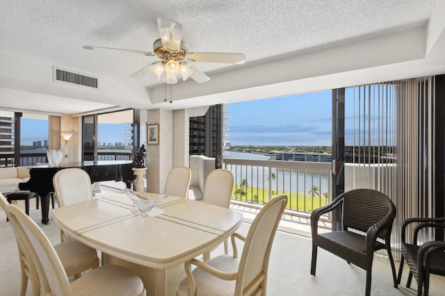 dining area featuring a wall of windows, a textured ceiling, a water view, and ceiling fan