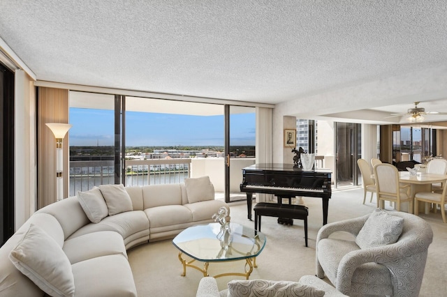 living room with a textured ceiling, ceiling fan, a wall of windows, a water view, and light colored carpet