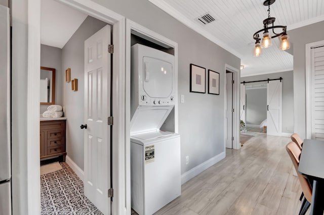 laundry room with light hardwood / wood-style flooring, a barn door, stacked washer and dryer, and crown molding