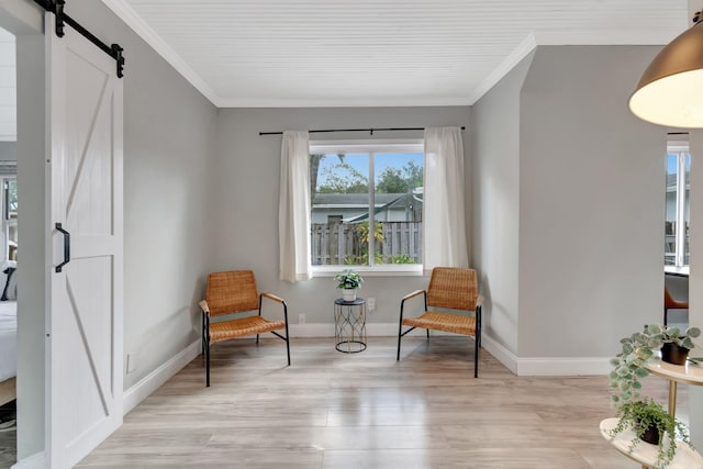 sitting room with a barn door, ornamental molding, and light wood-type flooring