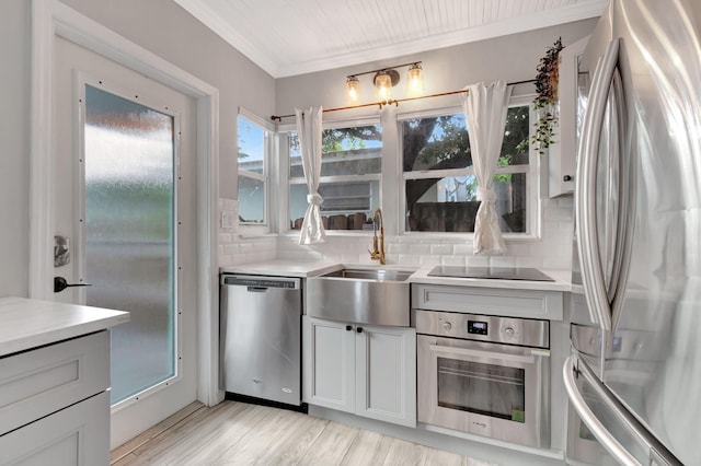 kitchen with stainless steel appliances, light wood-type flooring, sink, and tasteful backsplash