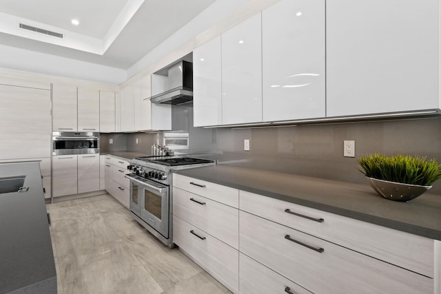 kitchen with dark countertops, visible vents, modern cabinets, wall chimney range hood, and appliances with stainless steel finishes