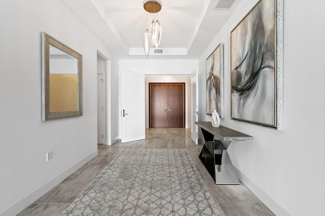 corridor with a raised ceiling, visible vents, baseboards, and a notable chandelier