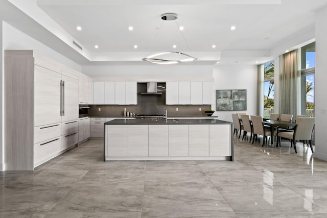 kitchen featuring dark countertops, an island with sink, modern cabinets, stainless steel oven, and wall chimney exhaust hood