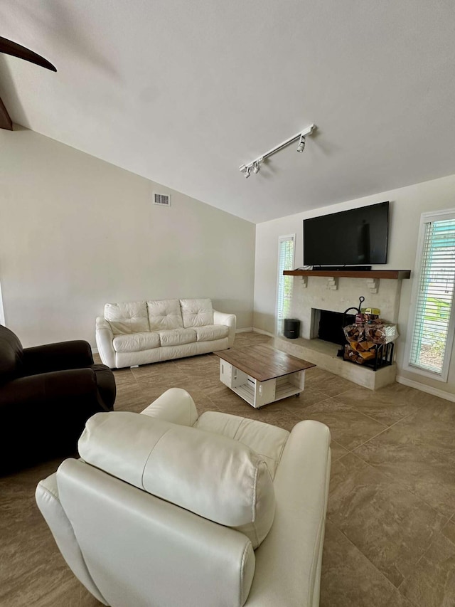 1121 SW Pine Tree Ln, Palm City, FL 34990 - living area with rail lighting, vaulted ceiling, a fireplace with raised hearth, baseboards, and ceiling fan
