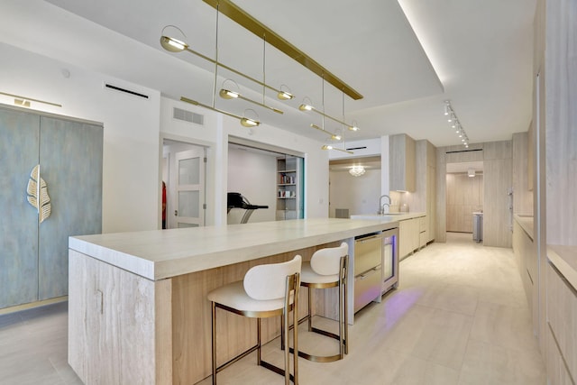 kitchen with sink, decorative light fixtures, track lighting, a breakfast bar, and light brown cabinetry