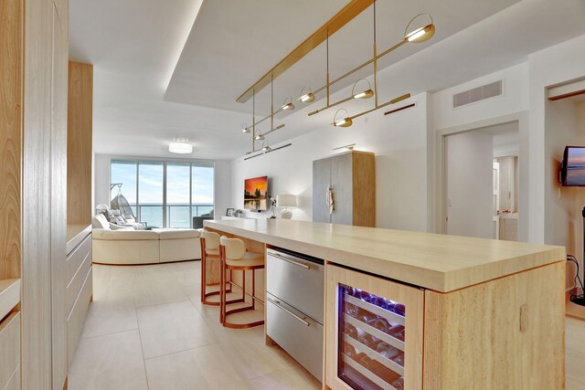 kitchen with a water view, light brown cabinetry, decorative light fixtures, and a kitchen breakfast bar