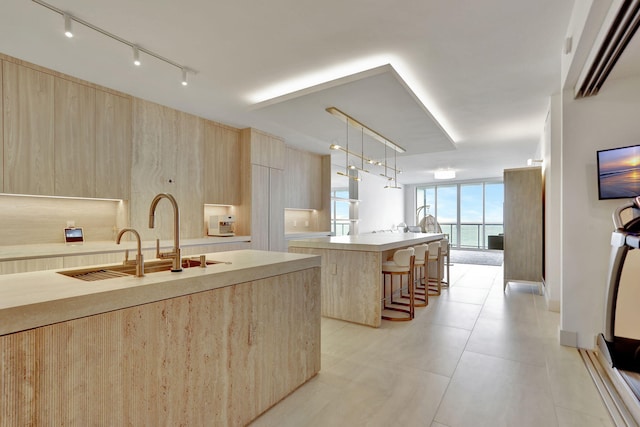 kitchen featuring light brown cabinets, hanging light fixtures, a kitchen island with sink, track lighting, and a kitchen bar