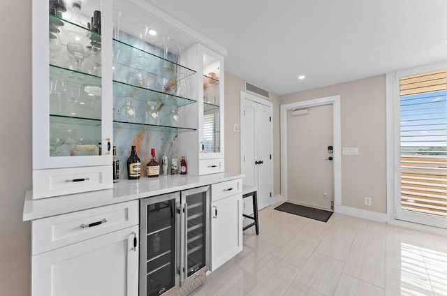 bar with plenty of natural light, white cabinets, and beverage cooler