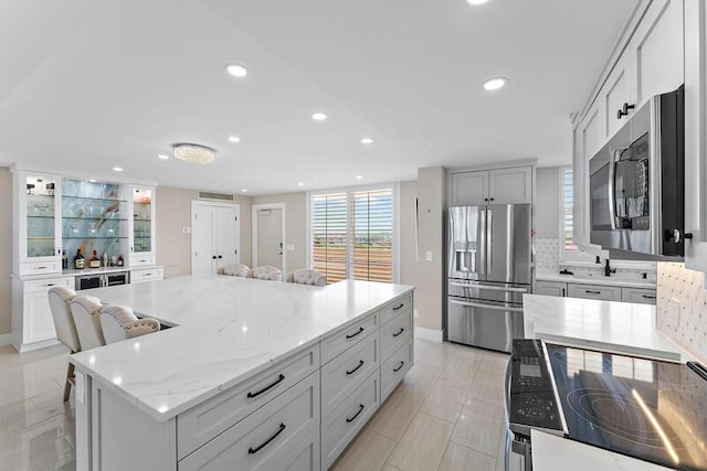 kitchen with stainless steel appliances, light stone counters, a breakfast bar area, decorative backsplash, and a kitchen island