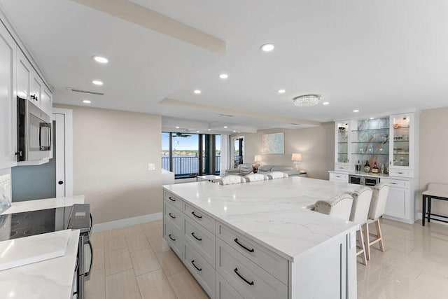 kitchen with a breakfast bar, a center island, white cabinetry, and light stone counters