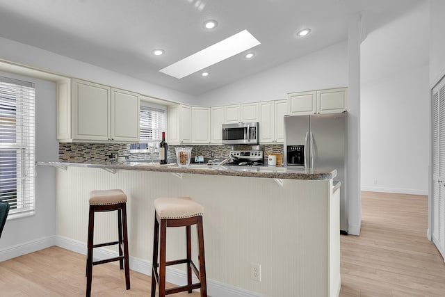 kitchen with stainless steel appliances, a kitchen bar, light wood-type flooring, and vaulted ceiling with skylight