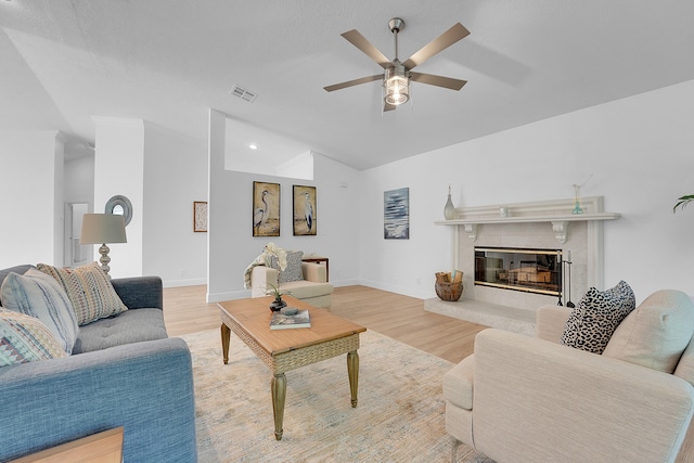 living room featuring light hardwood / wood-style floors, a fireplace, vaulted ceiling, and ceiling fan