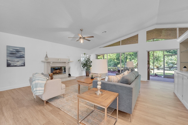 living room with light wood-type flooring, vaulted ceiling, ceiling fan, and a fireplace